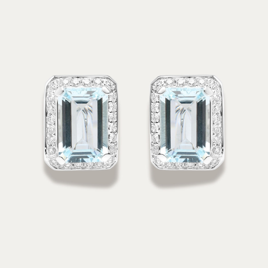 Pair of emerald-cut aquamarine gemstone 18K white gold earrings with diamond accents on a light gray background