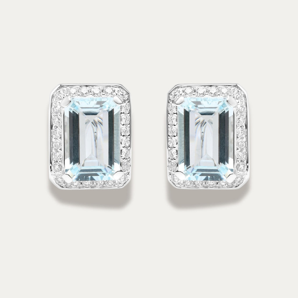 Pair of emerald-cut aquamarine gemstone 18K white gold earrings with diamond accents on a light gray background
