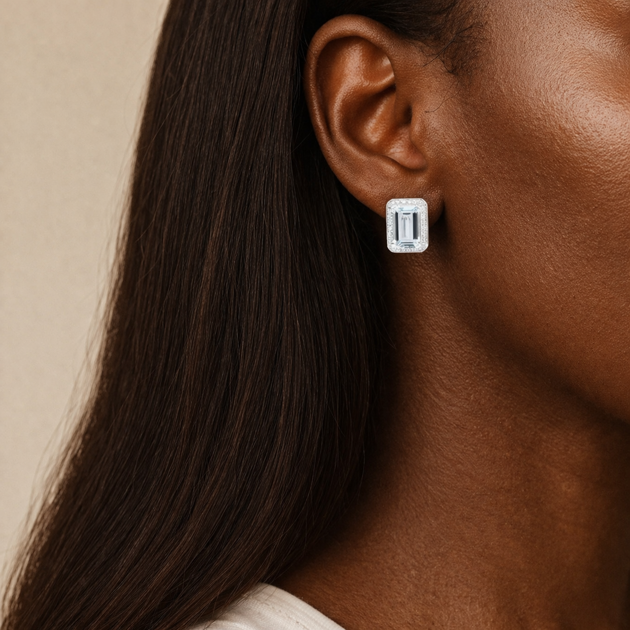 Close-up of a woman's ear wearing a aquamarine and diamond earring with a neutral background