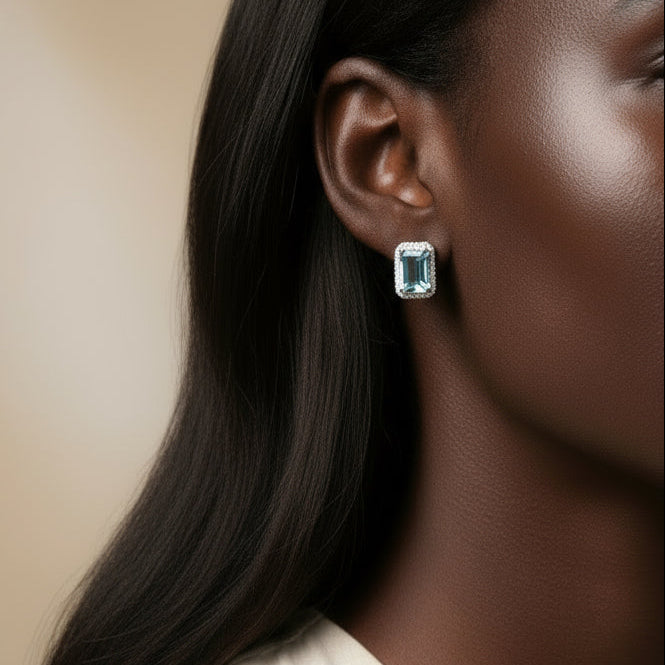 Close-up of a woman wearing aquamarine 18K white gold earrings with a beige background