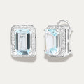 Pair of emerald-cut aquamarine gemstone 18K white gold earrings with diamond accents on a light gray background