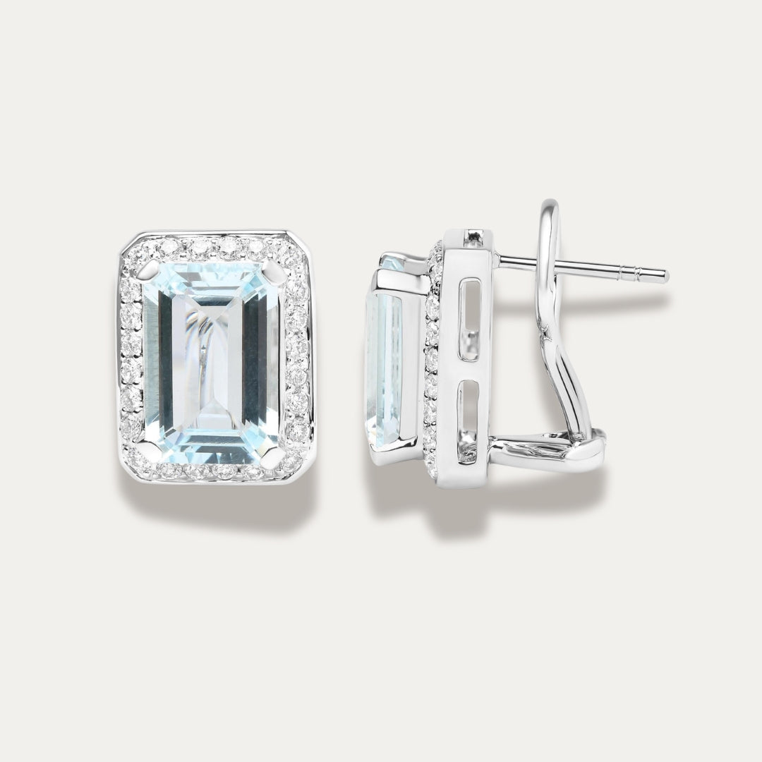 Pair of emerald-cut aquamarine gemstone 18K white gold earrings with diamond accents on a light gray background