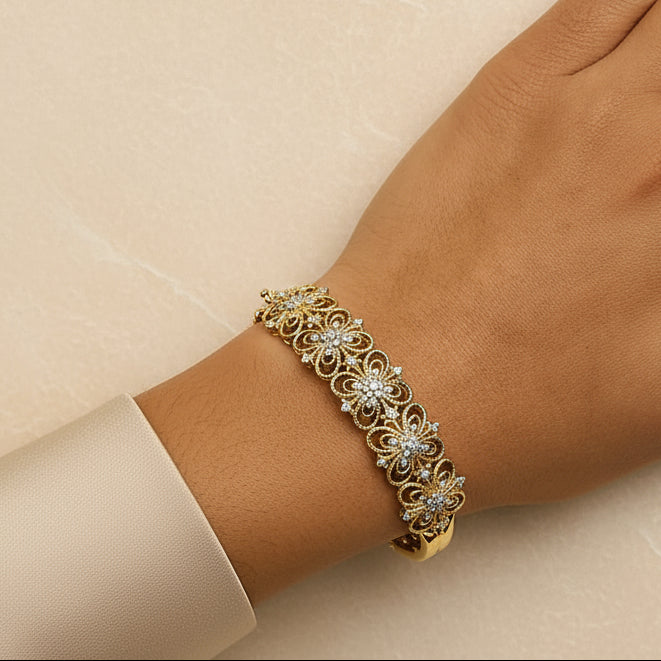 Gold bracelet with floral design on a wrist against a beige background