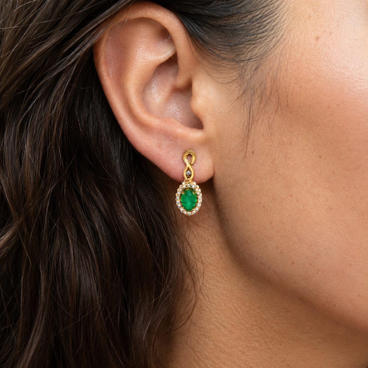 Close-up of a woman's ear wearing a gold and emerald green earring.