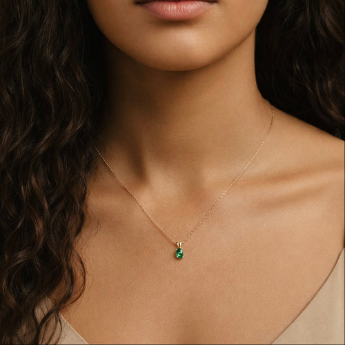 Model wearing the Esmé Solitaire Pendant Necklace by Teraju, featuring a green emerald in 14K yellow gold on an 18-inch rope chain.