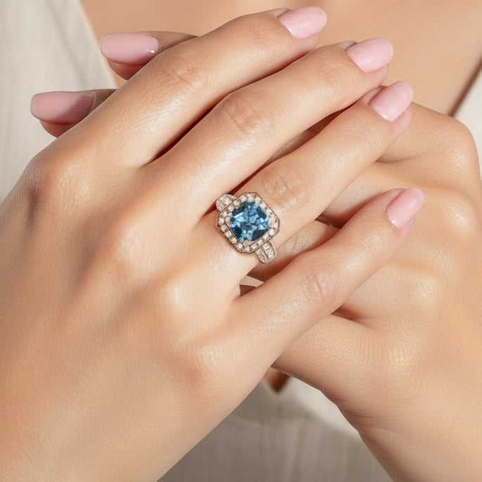 Close-up of a hand wearing a ring with a blue aquamarine gemstone on a neutral background