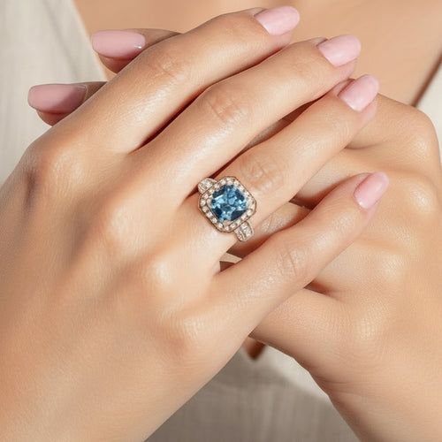 Close-up of a hand wearing a ring with a blue aquamarine gemstone on a neutral background