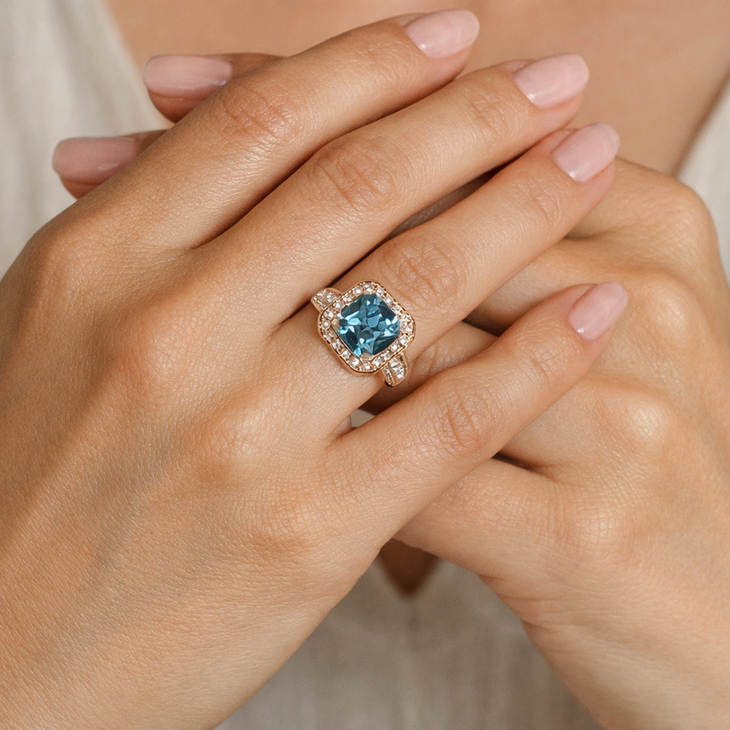 Close-up of a hand wearing a ring with a blue aquamarine gemstone on a neutral background