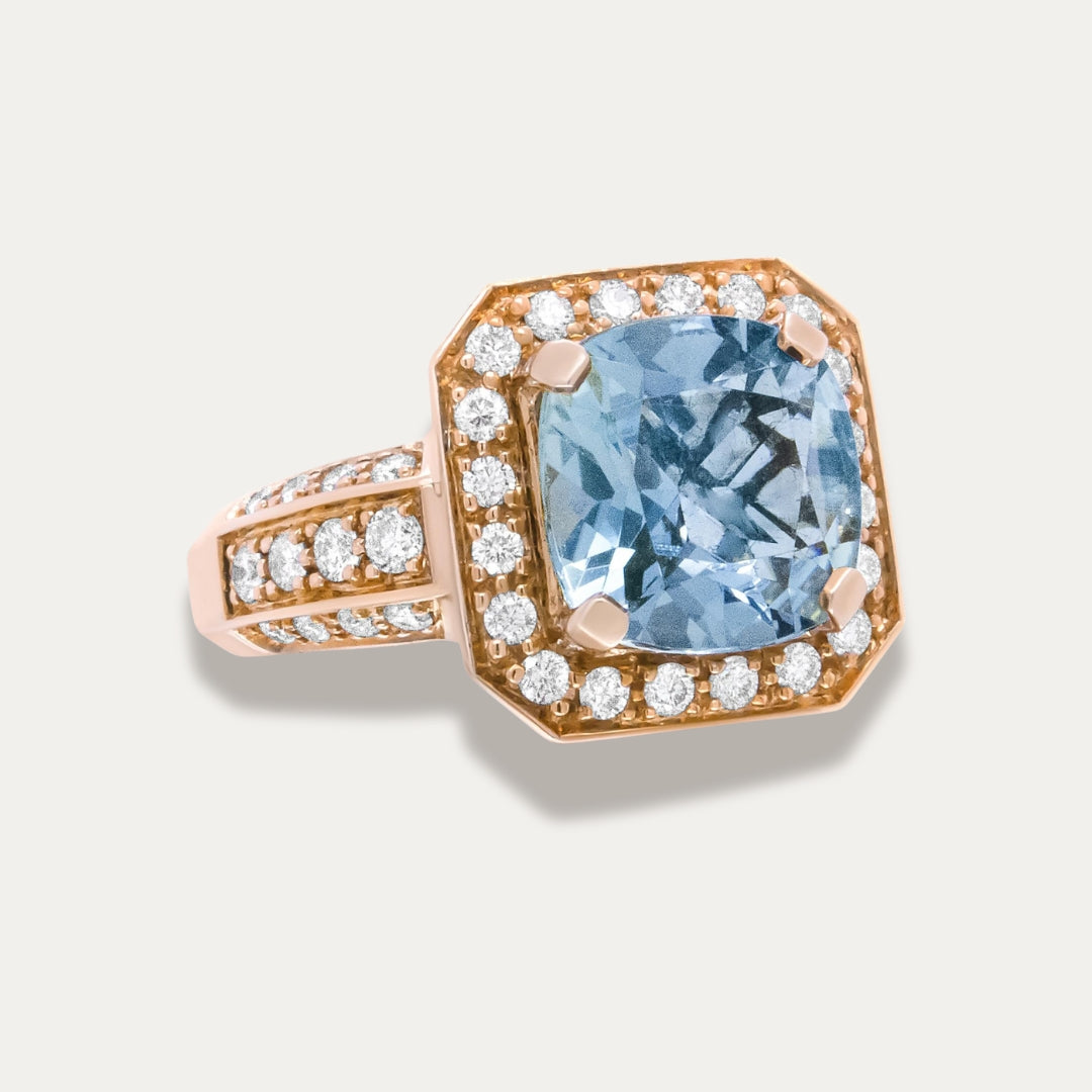 Ring with blue aquamarine gemstone and 18K rose gold band on a light gray background