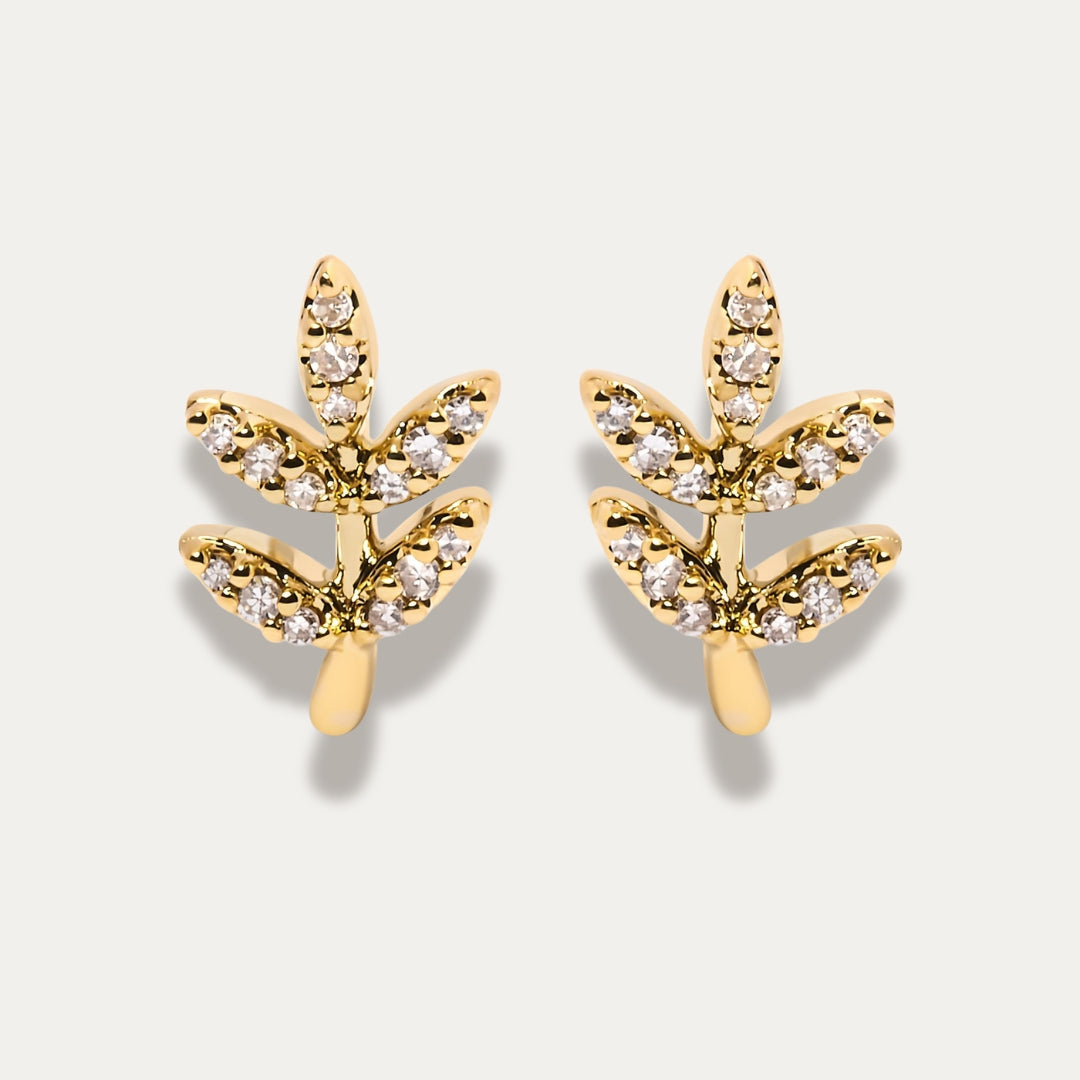 Gold leaf-shaped earrings with diamond-like stones on a light gray background