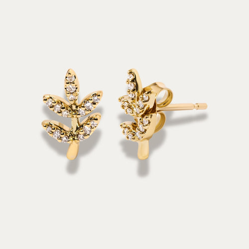 Gold leaf-shaped earrings with embedded stones on a light beige background