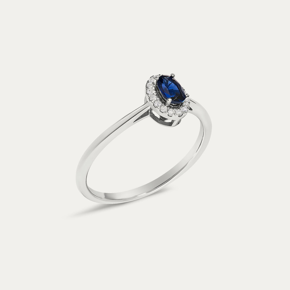 Angled view of the Origine birthstone halo ring in 10K white gold with an oval blue sapphire and its halo of natural diamonds