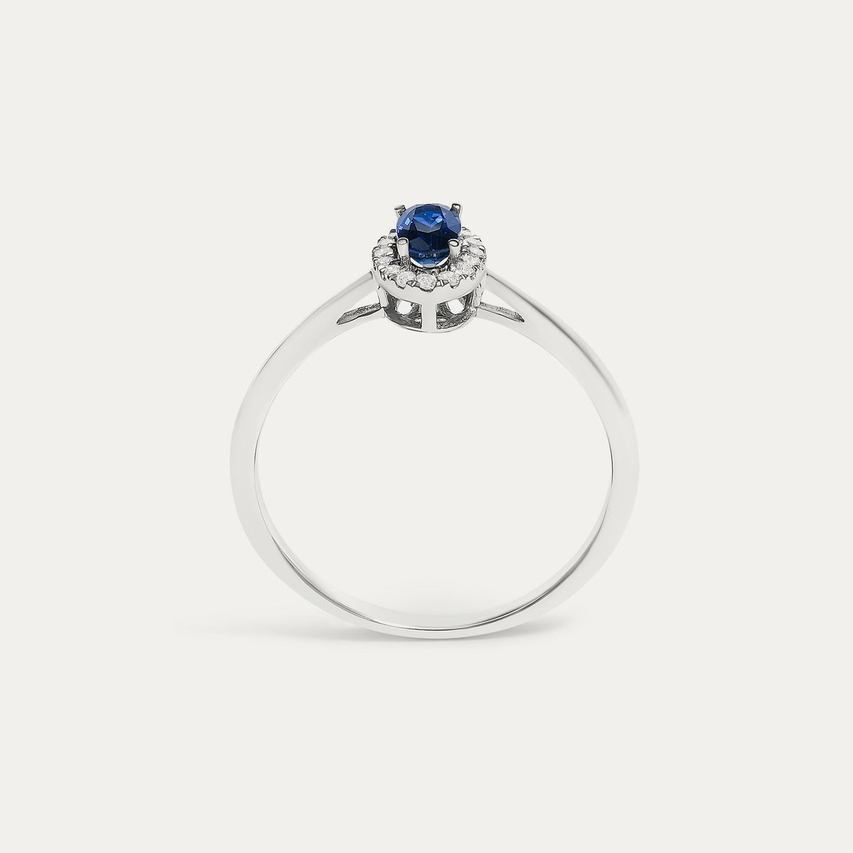 Face view of the Origine birthstone halo ring in 10K white gold with an oval blue sapphire crowned by a halo of natural diamonds