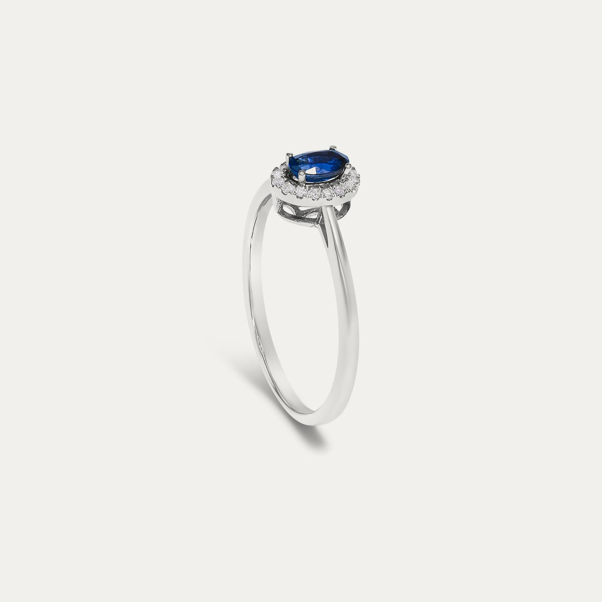 Profile view of the Origine birthstone halo ring in 10K white gold showing the raised halo setting with an oval blue sapphire above the slim band