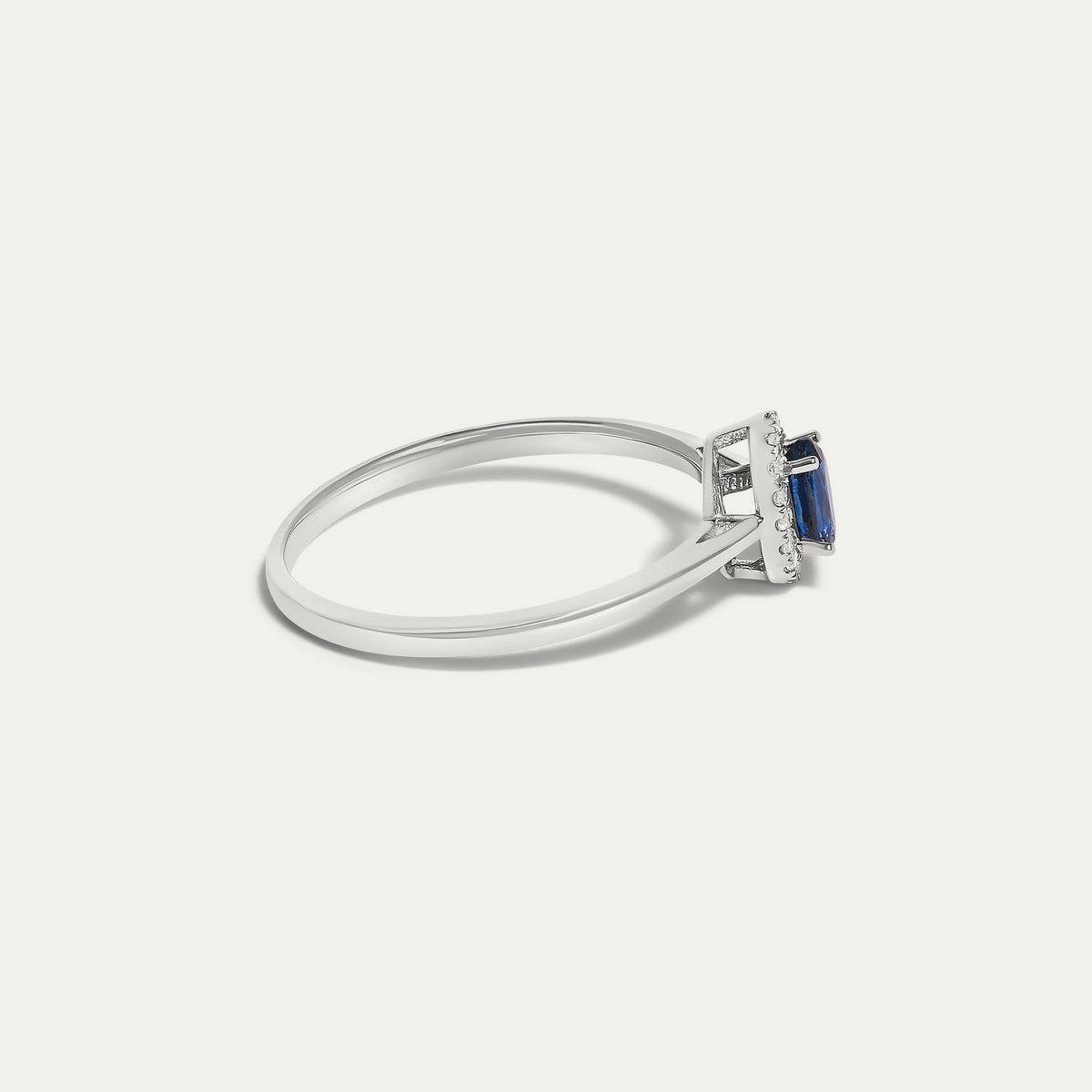 Side view of the Origine birthstone halo ring in 10K white gold with an oval blue sapphire and a halo of natural diamonds above the slim band