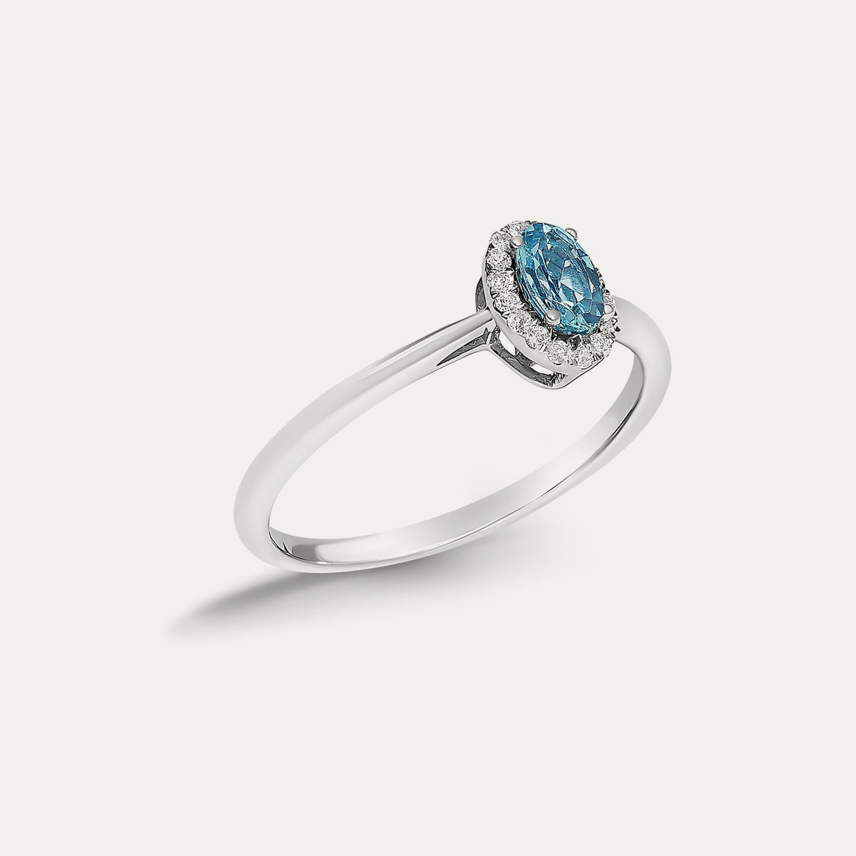Angled view of the Origine birthstone halo ring in 10K white gold with an oval blue topaz and its halo of natural diamonds
