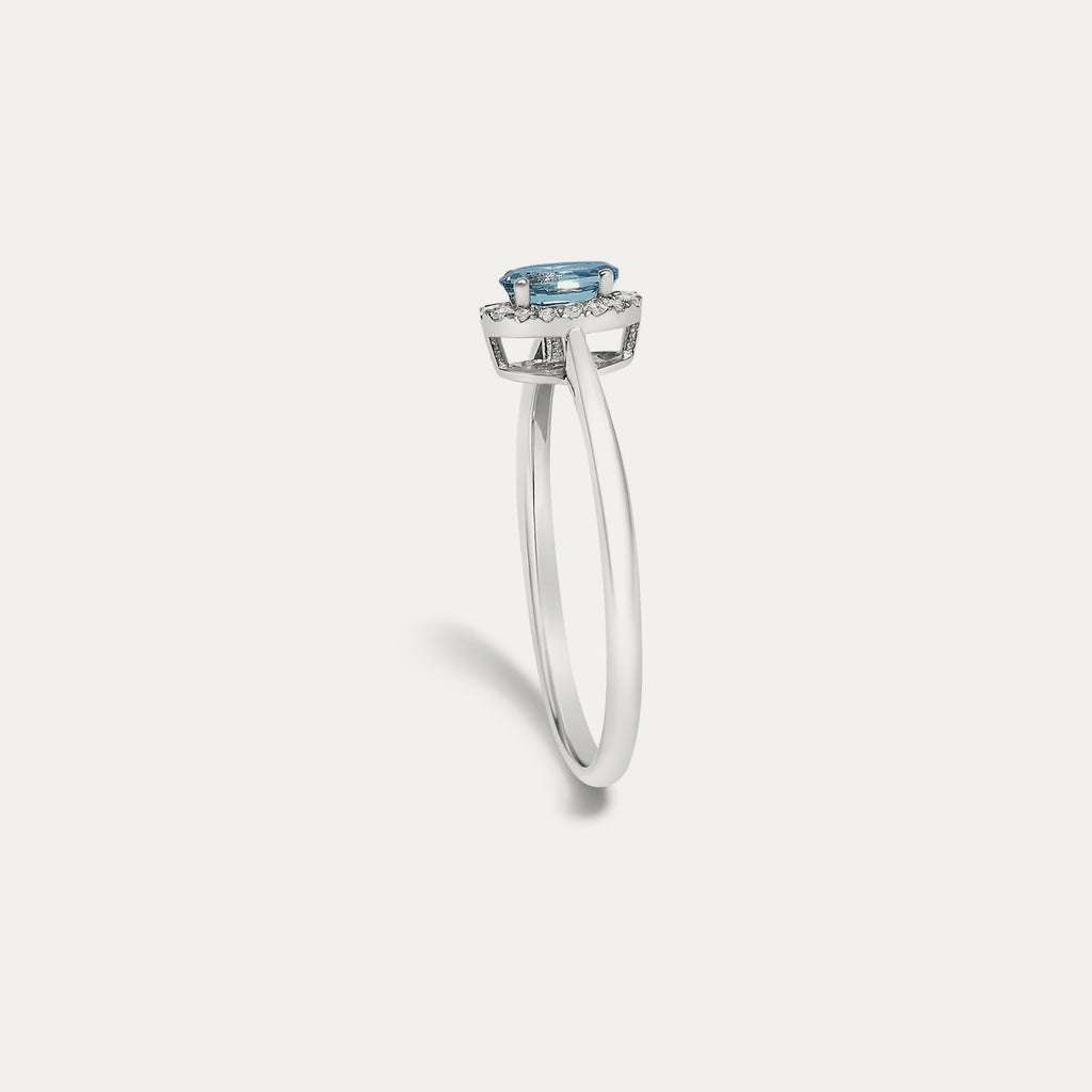 Profile view of the Origine birthstone halo ring in 10K white gold showing the raised halo setting with an oval blue topaz above the slim band