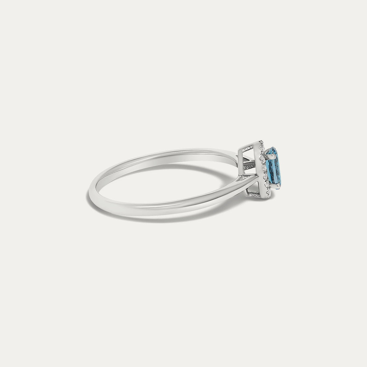 Side view of the Origine birthstone halo ring in 10K white gold with an oval blue topaz and a halo of natural diamonds above the slim band