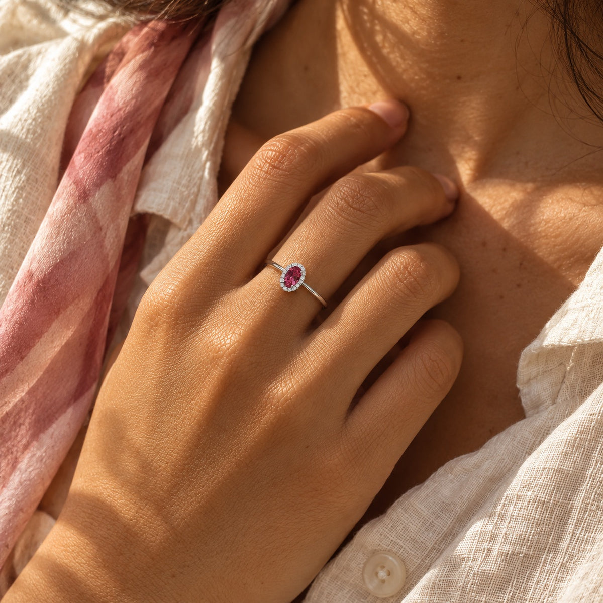 The Origine birthstone halo ring with an oval pink tourmaline and a halo of natural diamonds, worn on the hand in natural light