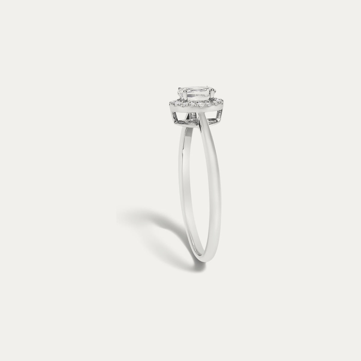 Profile view of the Origine birthstone halo ring in 10K white gold showing the raised halo setting with an oval white topaz above the slim band