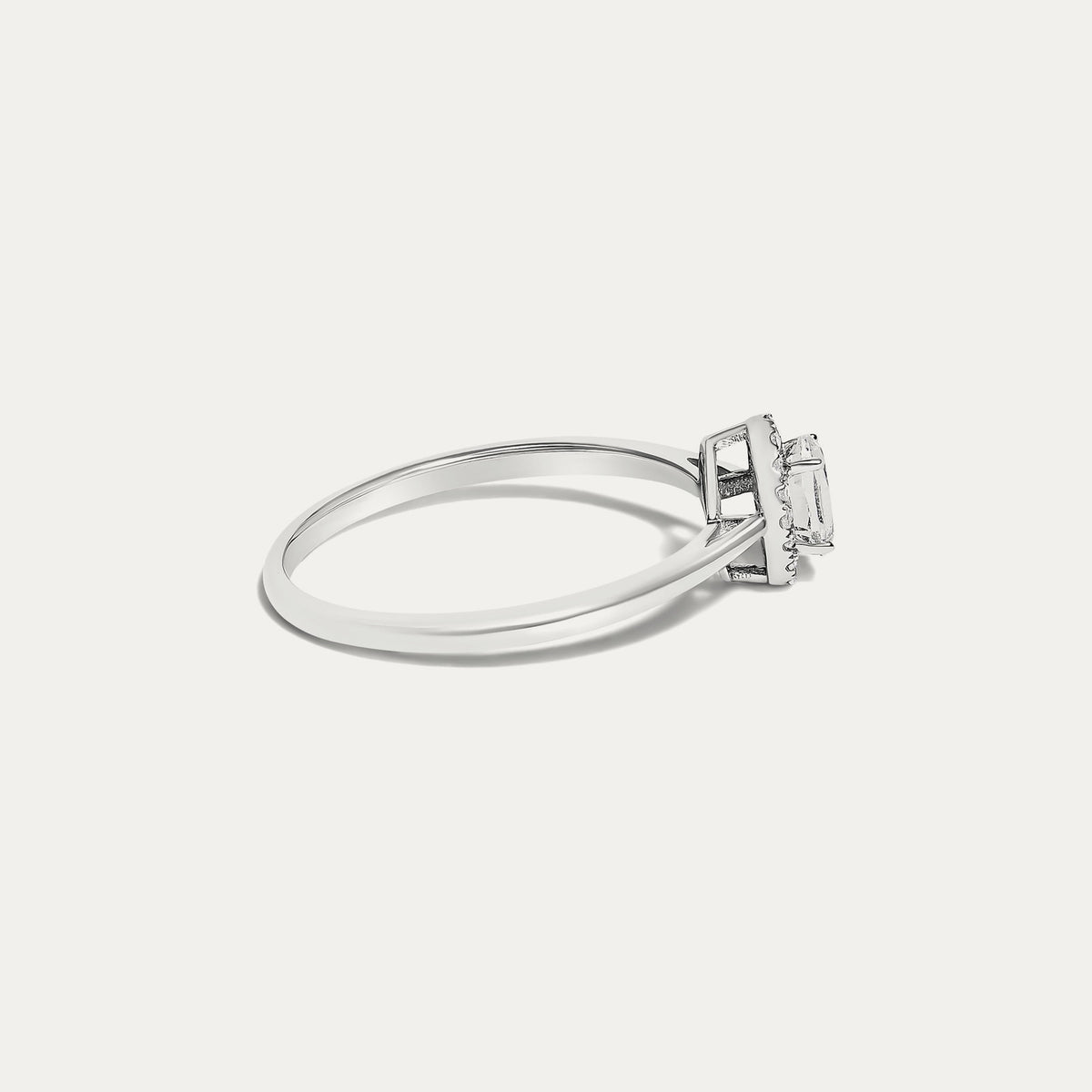 Side view of the Origine birthstone halo ring in 10K white gold with an oval white topaz and a halo of natural diamonds above the slim band