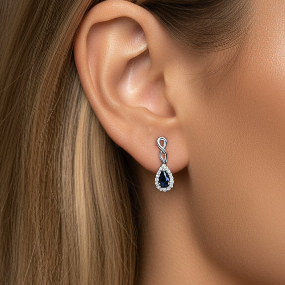 Close-up of a woman wearing a white gold earring with sapphire gemstones on a grey background