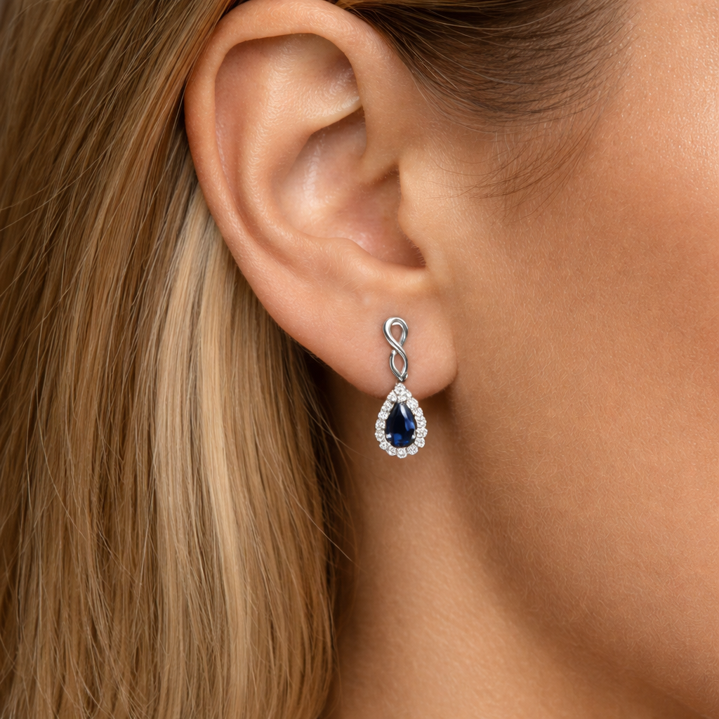 Close-up of a woman wearing a white gold earring with sapphire gemstones on a grey background