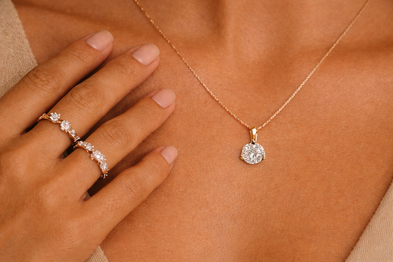 Yellow gold ring and diamond necklace on a person's hand against a brown background