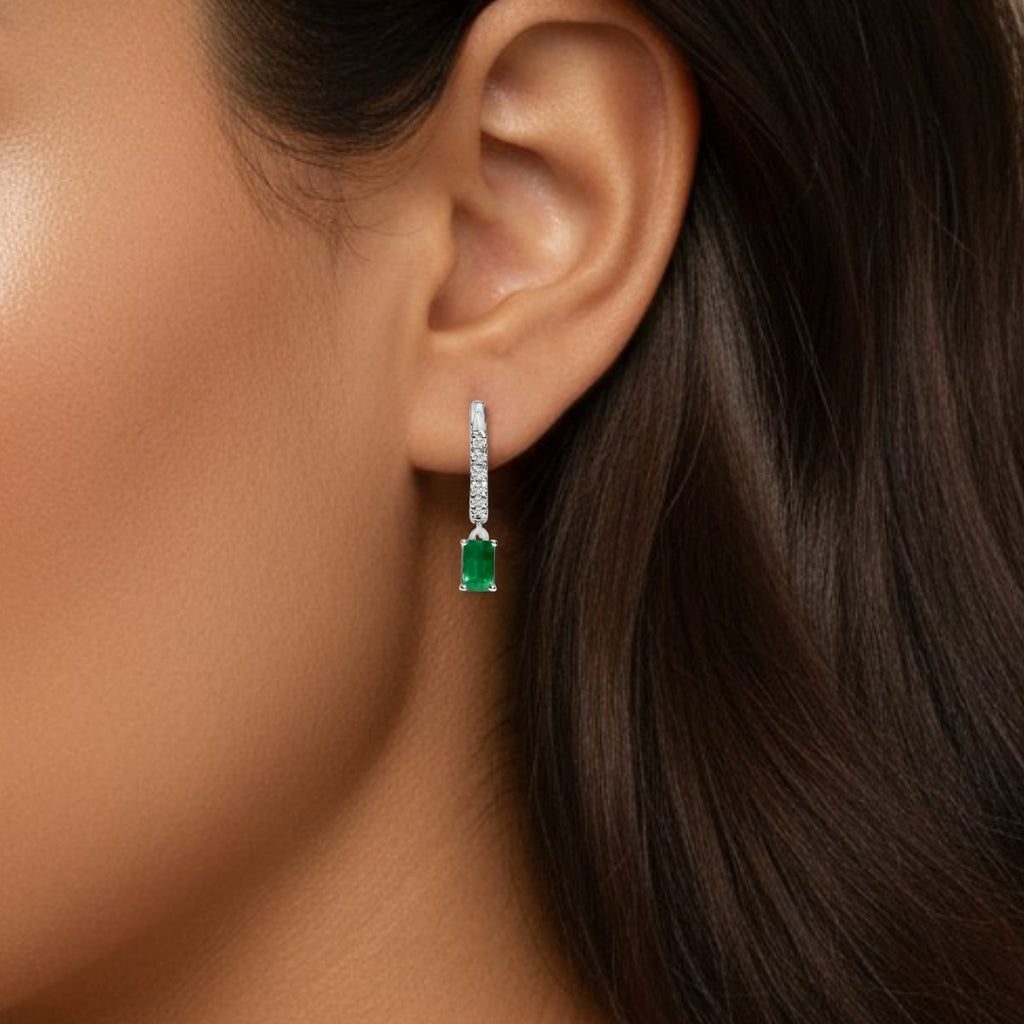 Close-up of an ear wearing a green emerald earring with a beige background