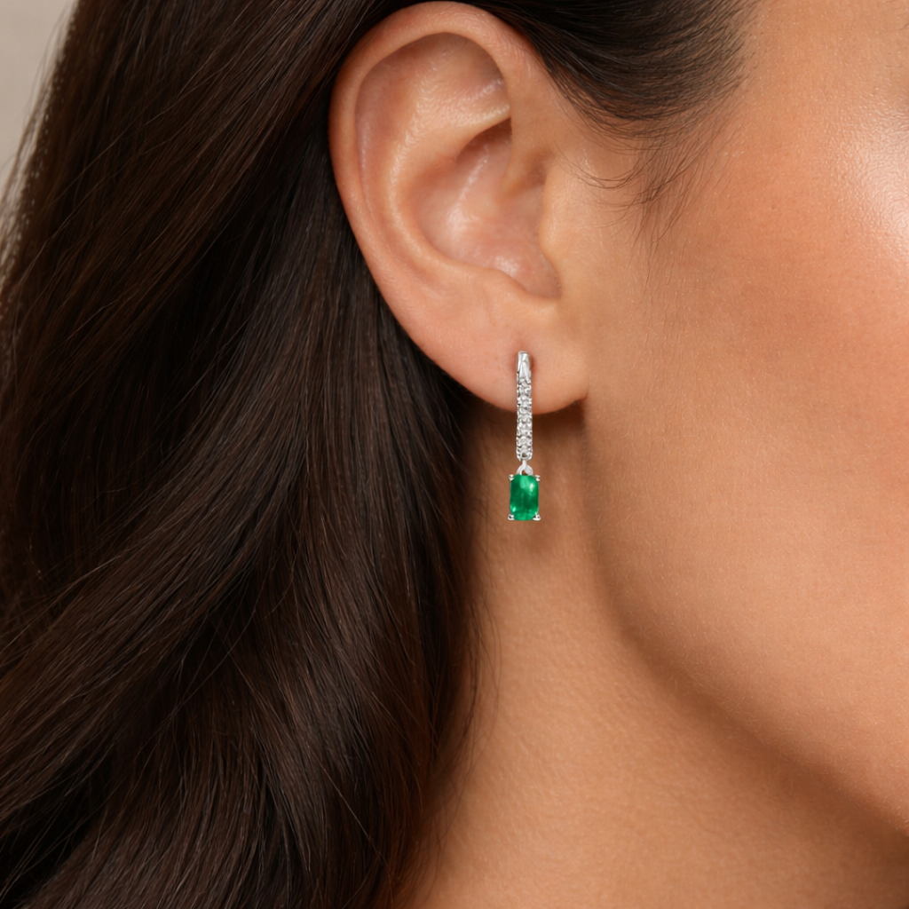 Close-up of an ear wearing a green emerald earring with a beige background