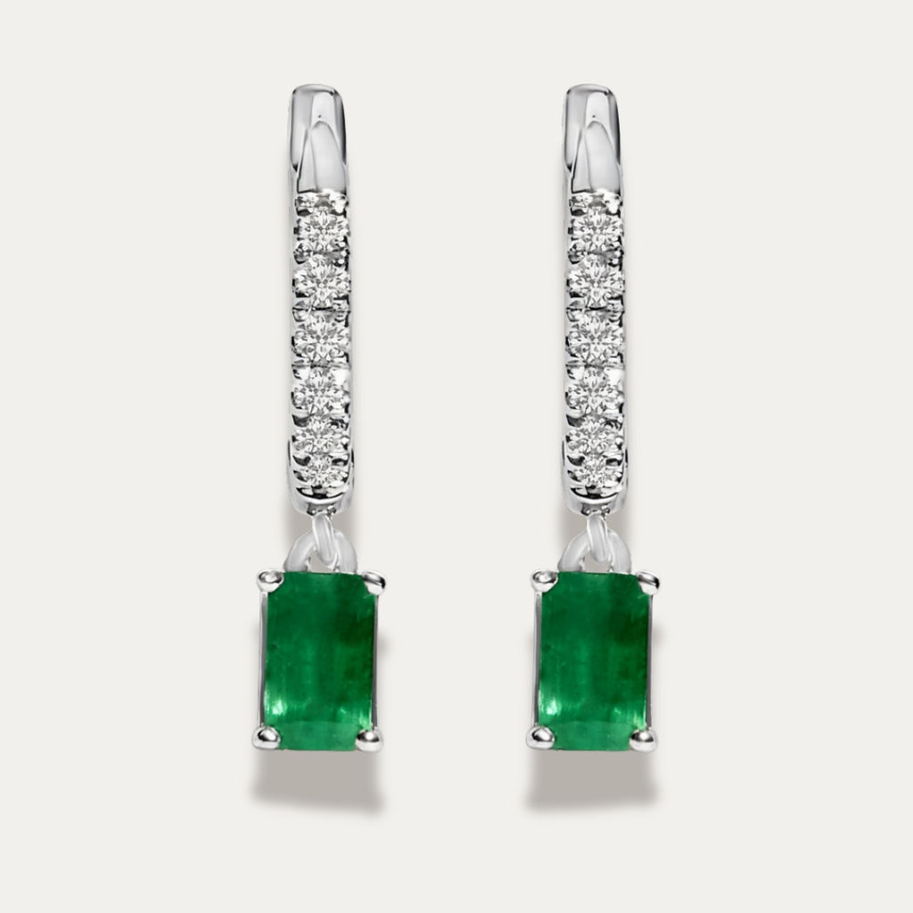 Pair of silver earrings with green emerald gemstones on a light grey background