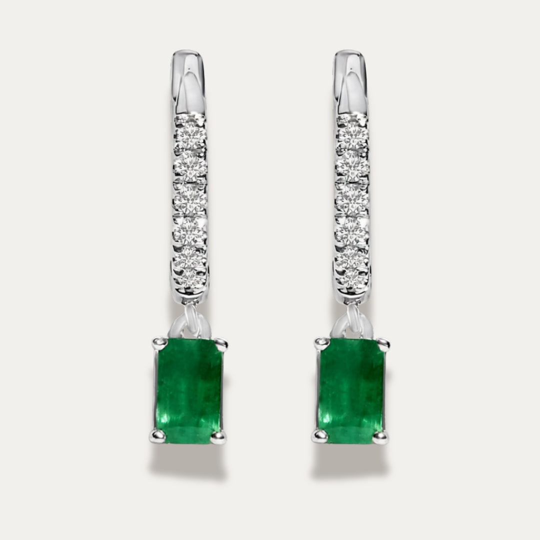 Pair of silver earrings with green emerald gemstones on a light grey background