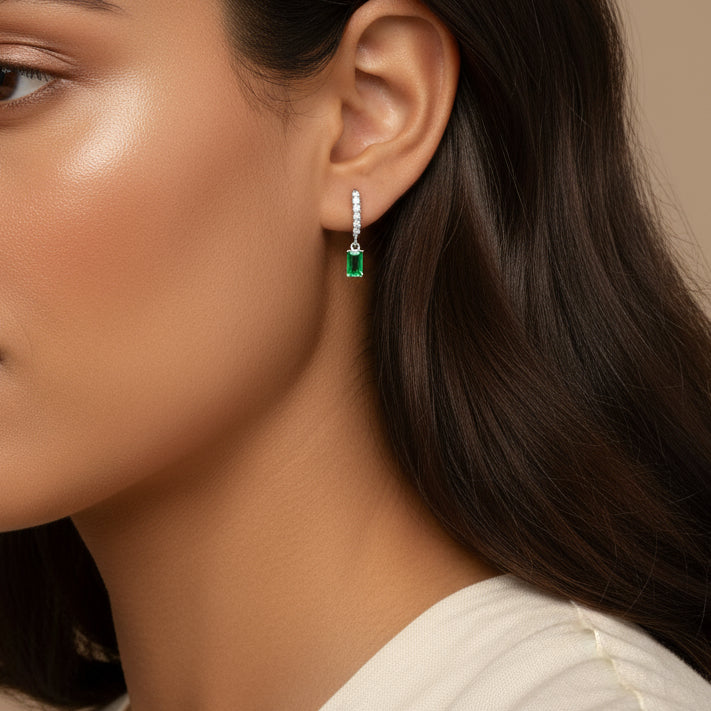 Close-up of a woman wearing a green emerald earring with a beige background