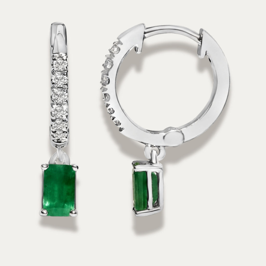 Pair of silver earrings with green emerald gemstones on a light grey background