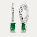 Pair of white gold earrings with green emerald gemstones on a light grey background