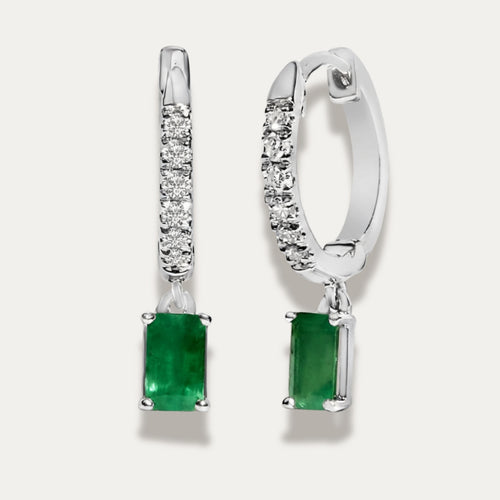 Pair of white gold earrings with green emerald gemstones on a light grey background