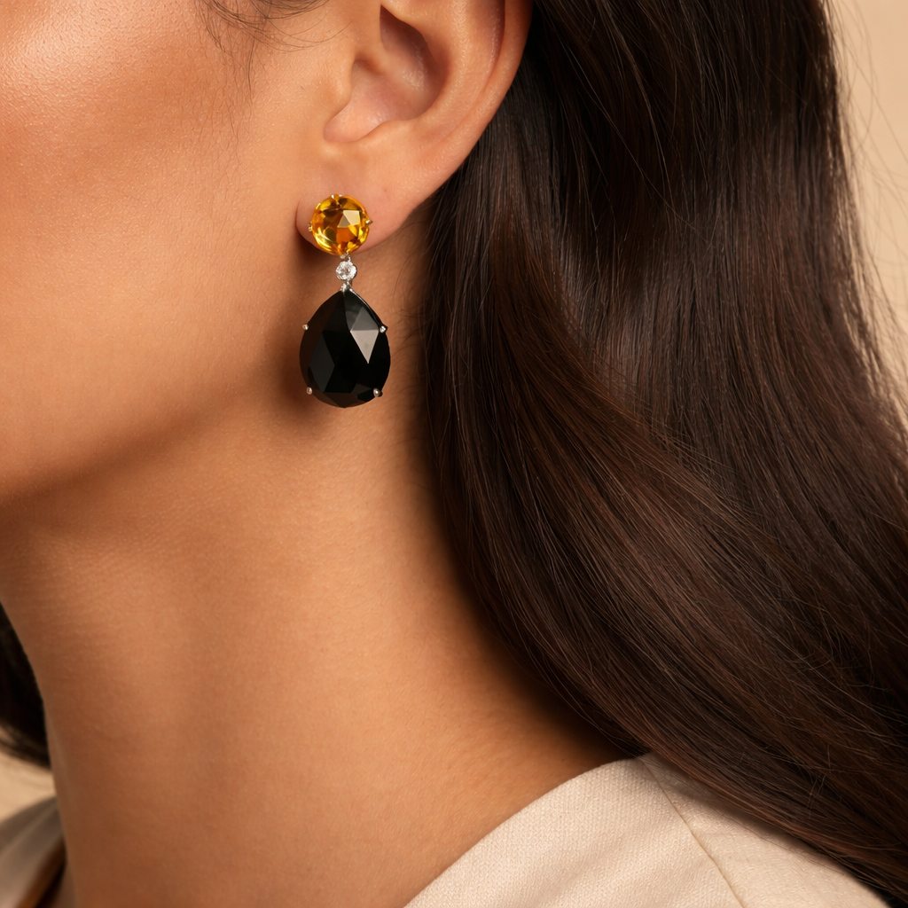 Amara dangle earrings in 18K white and yellow gold featuring pear-cut black onyx, round yellow citrine, and a white diamond, elegantly worn on a woman's ear