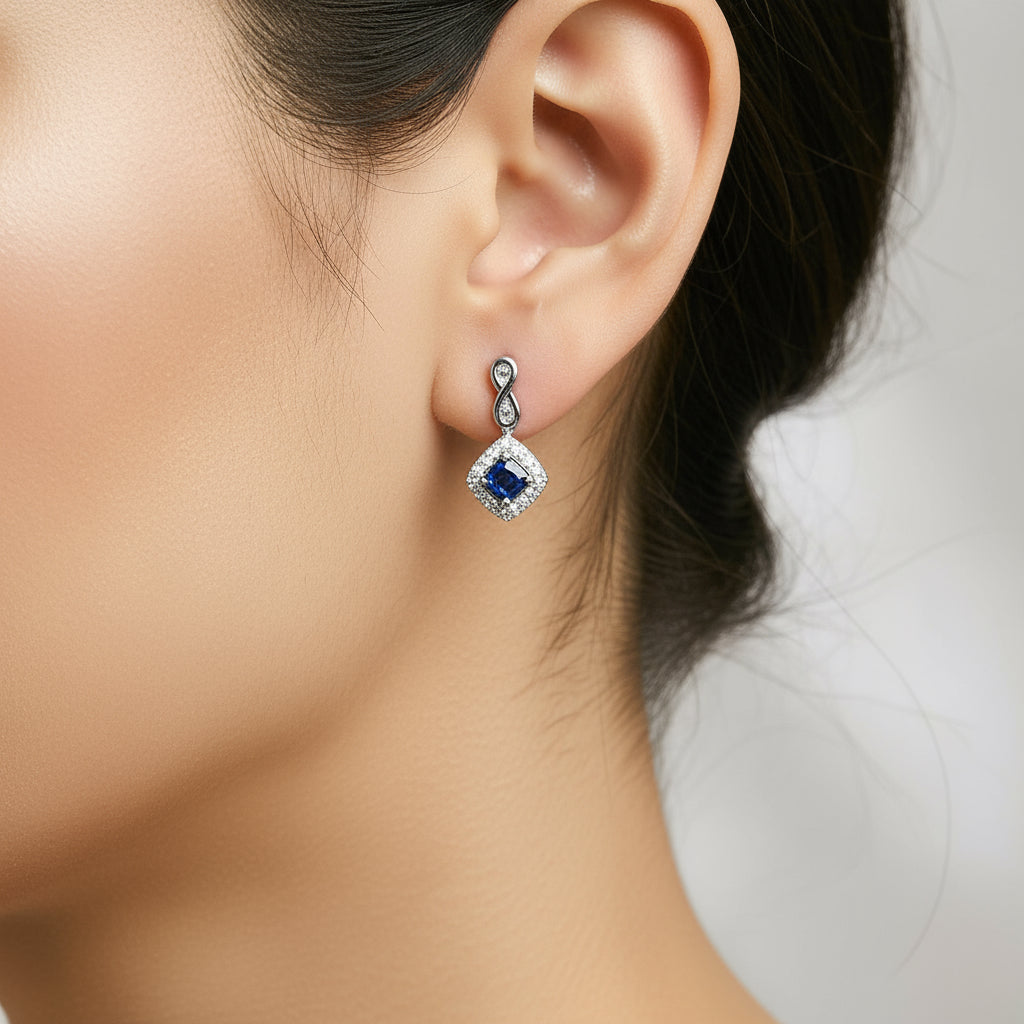 Model wearing Azur Halo cushion-shaped drop earrings featuring blue sapphire and diamond halo in 10K white gold