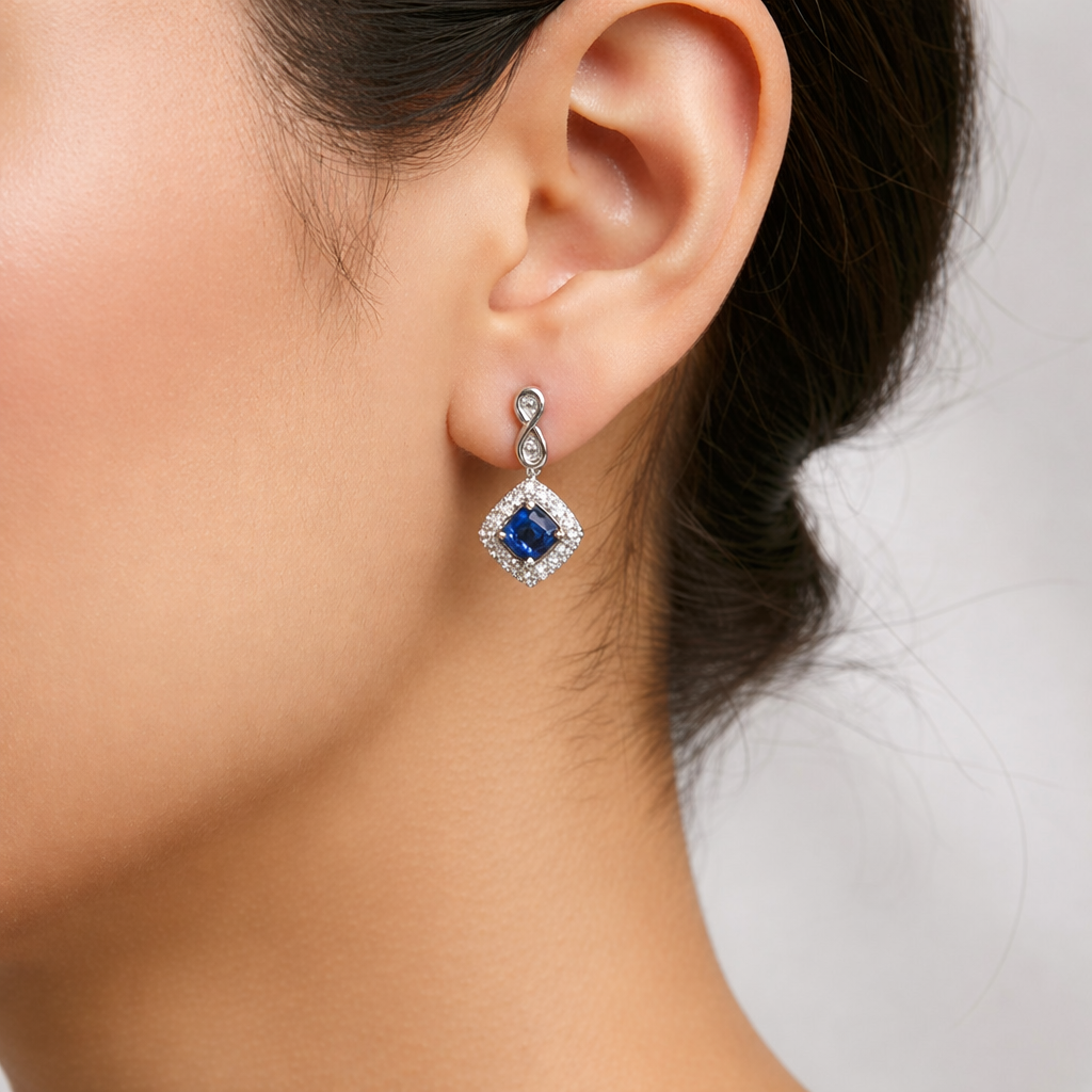 Model wearing Azur Halo cushion-shaped drop earrings featuring blue sapphire and diamond halo in 10K white gold