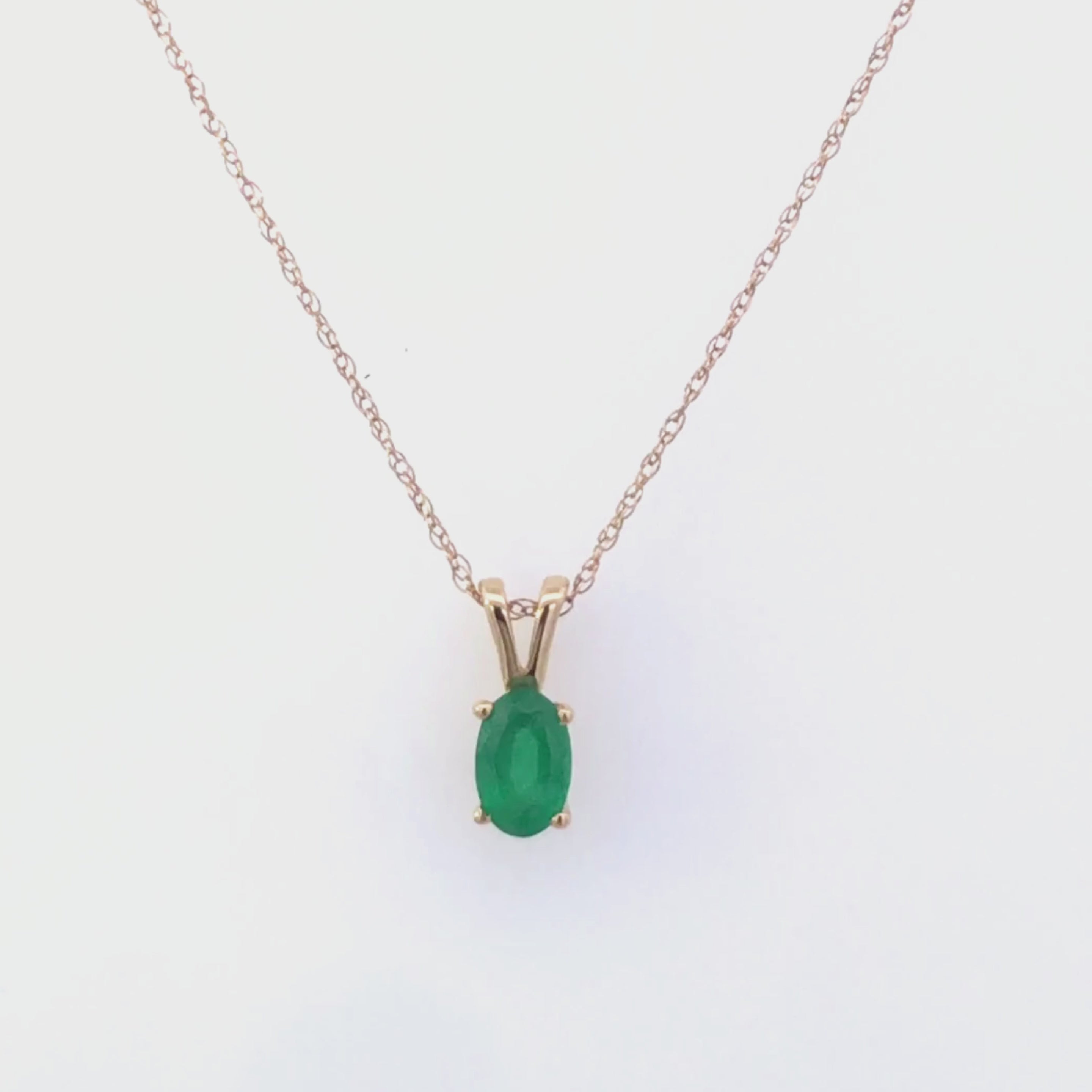 Video of gold necklace with a emerald green gemstone pendant on a white background