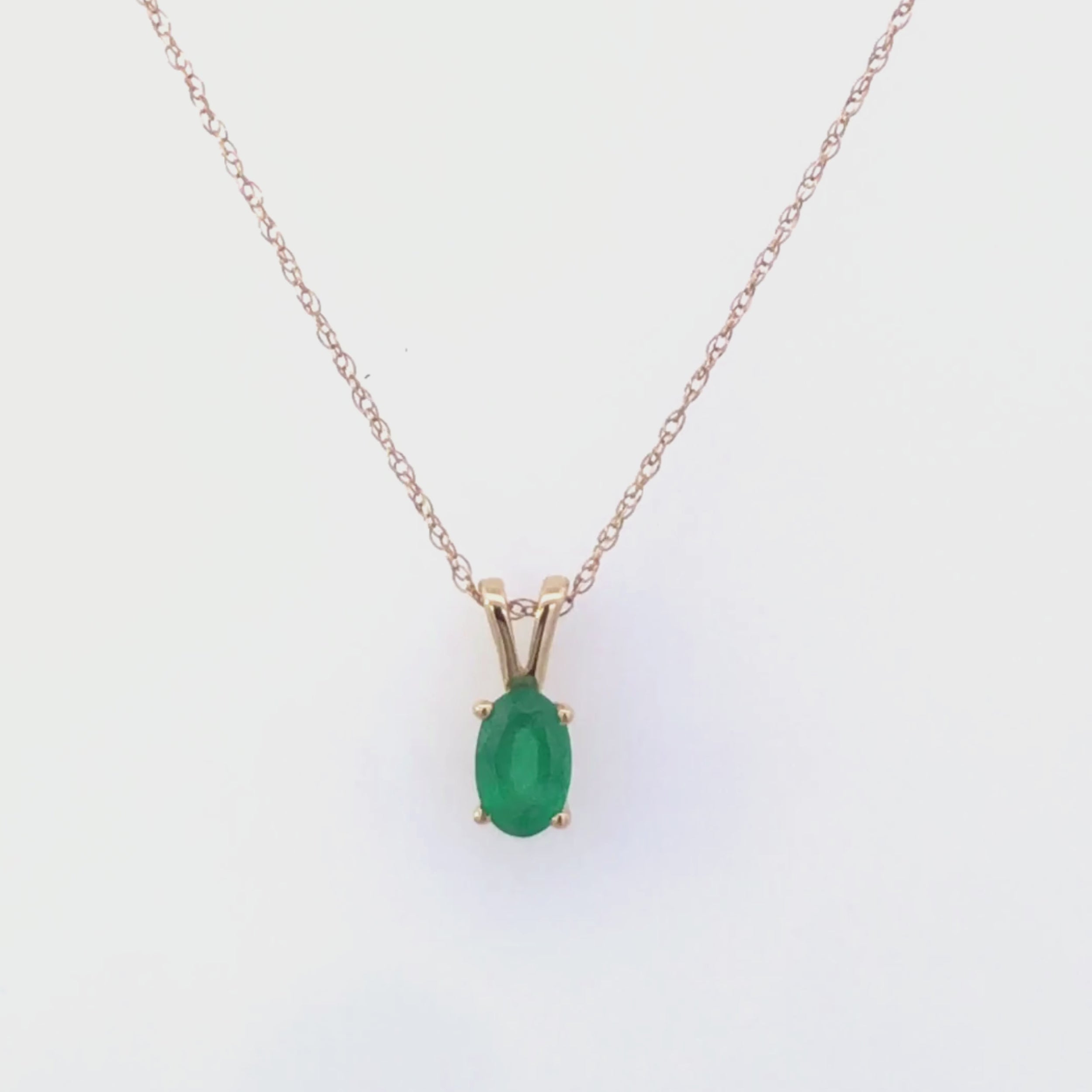 Video of gold necklace with a emerald green gemstone pendant on a white background