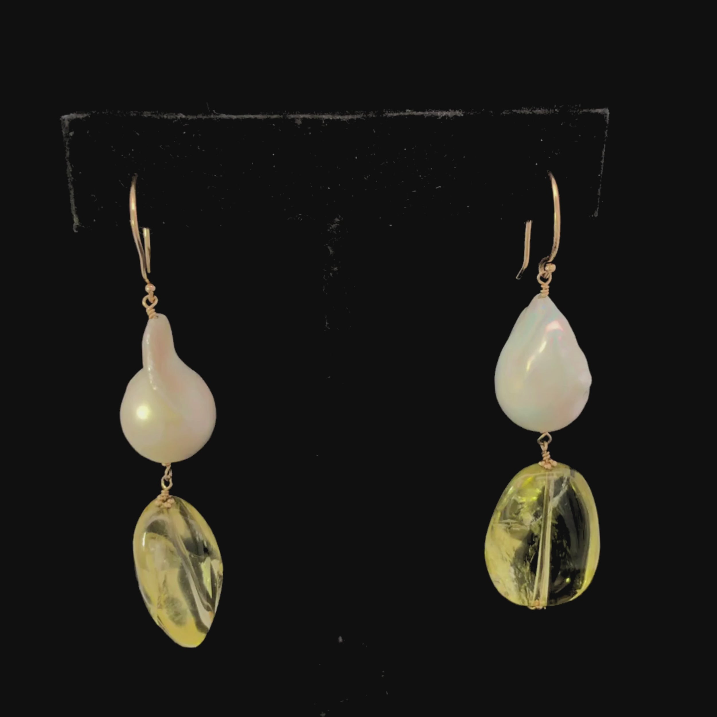 Video of pair of earrings with large pearl and yellow citrine on a black background