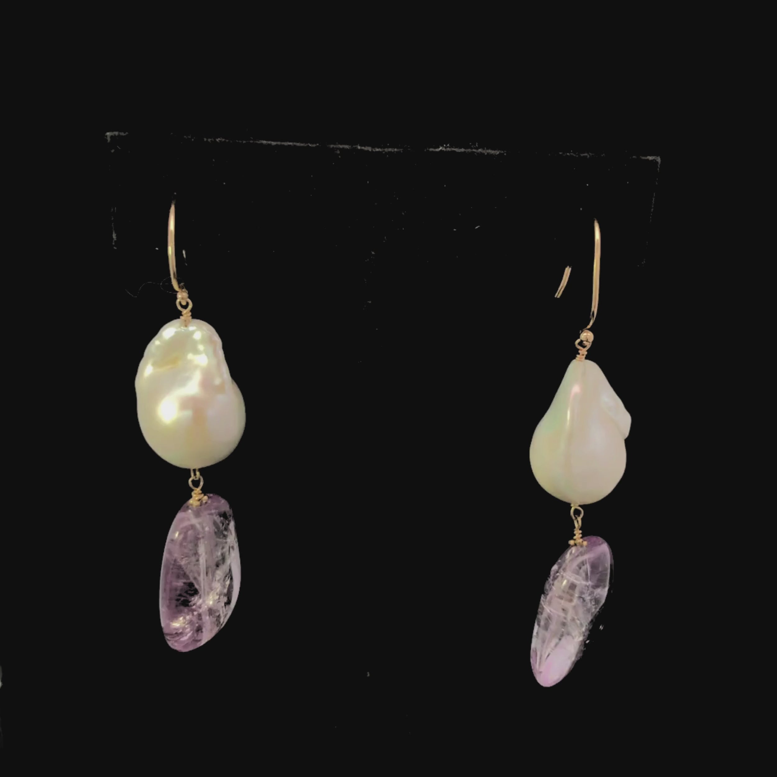 Video of pair of earrings with gold hooks, pearl and amethyst purple teardrop on a black background